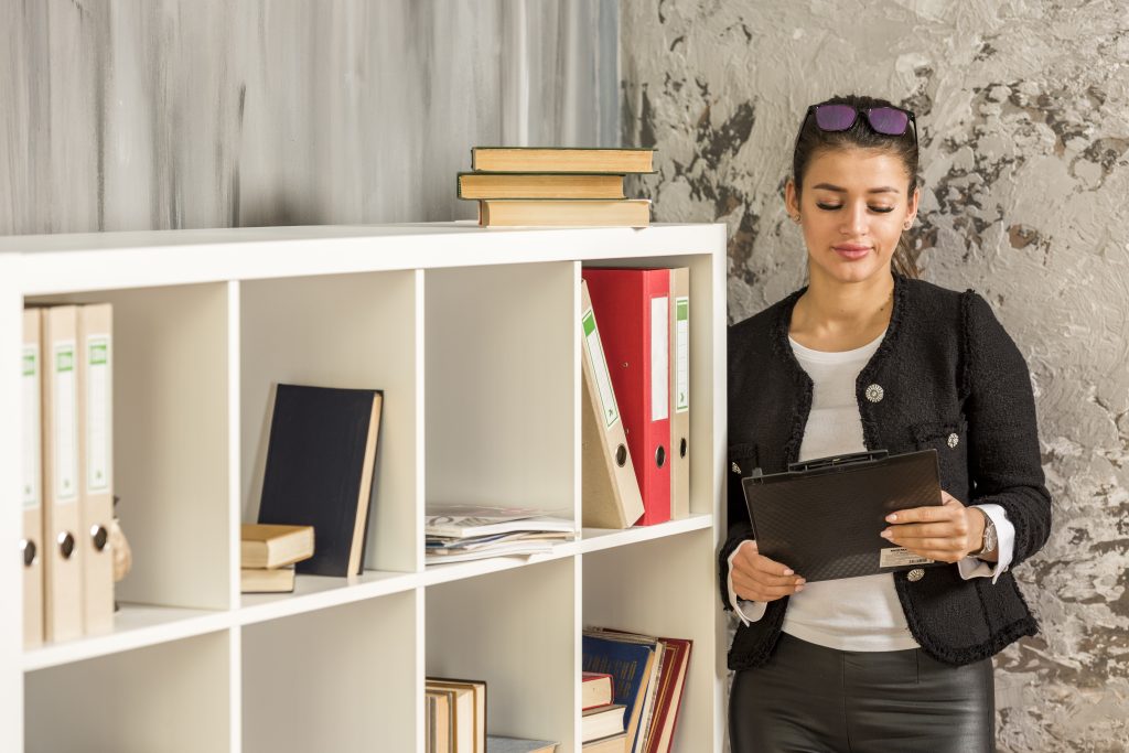 biały regał na książki obok niego kobieta która coś czyta