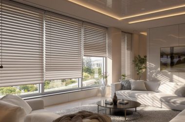 Nowoczesny salon z dużymi oknami i roletami, narożna sofa w jasnym kolorze, stolik kawowy i dekoracyjne dodatki – aranżacja wnętrza z meblami o minimalistycznym designie.