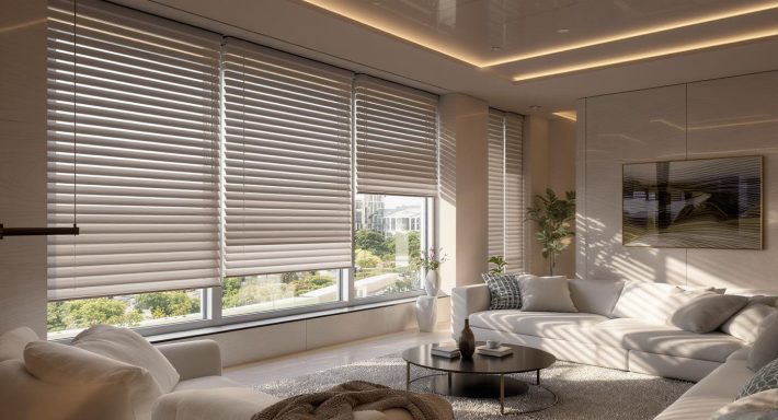 Nowoczesny salon z dużymi oknami i roletami, narożna sofa w jasnym kolorze, stolik kawowy i dekoracyjne dodatki – aranżacja wnętrza z meblami o minimalistycznym designie.